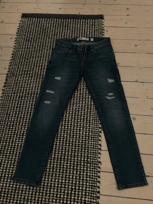 Mörkblå  jeans från Incode - Säljer ett par mörkblå  jeans från Incode med slitningar på låren och knäna. Jeansen har klassisk femficksmodell, bälteshällor och dragkedjegylf. Perfekta för en trendig och avslappnad stil.