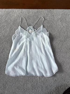 Ljusblå linnetopp från Zadig & Voltaire - Supersöt ljusblå linnetopp från Zadig & Voltaire med tunna axelband och spetsdetaljer längs urringningen. NYPRIS: över 2000kr. Toppen har en v-ringad form och är perfekt för varma dagar eller lager på lager. Materialet känns lätt och svalt.