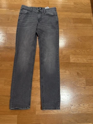 Grå slim fit jeans från Jack & Jones - Snygga grå slim fit jeans från Jack & Jones med klassisk femficksdesign och bälteshällor. Jeansen har raka ben och är tillverkade i ett mjukt denimtyg som ger en bekväm känsla. Perfekta för en avslappnad och trendig stil.