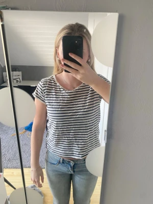 Randig vit och svart t-shirt - Säljer en klassisk vit t-shirt med svarta horisontella ränder. T-shirten har korta ärmar och rund halsringning. Perfekt till jeans eller shorts. 