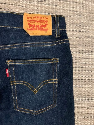 Levi's 512 Slim mörkblå denimjeans - Levi's 512 Slim jeans i mörkblå denim med klassisk femficksdesign, kontrastsömmar och röd Levi's-tag på bakfickan. Jeansen har hög midja och smal passform, tillverkade i slitstarkt bomullsdenim för en tidlös look.