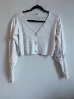 Vit långärmad tröja med knappar - Snygg v-ringad basic tröja från missguided med knappar. Något croppad, strl 34. Ribbad med snygga ärmar som smalnar av vid handlederna. 