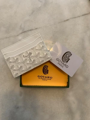 Vit kortfodral från Goy4ard - Snyggt vitt kortfodral från Goy4ard med det klassiska mönstret och loggan framtill. Fodralet har flera fack för kort och är tillverkat i exklusivt läder. Perfekt för dig som vill ha en stilren och lyxig accessoar i fickan.
