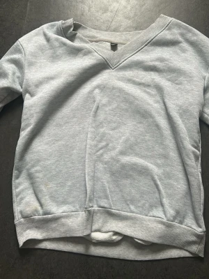 Ljusgrå sweatshirt med V-ringning - En enkel ljusgrå sweatshirt från H&M med V-ringad hals och ribbade muddar. Tröjan har en avslappnad passform och är tillverkad i mjukt bomullsmaterial. Perfekt för en chill och stilren look.