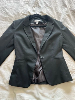 Svart klassisk kavaj med knapp - Snygg svart kavaj med en knapp framtill och två fickor. Kavajen har figurnära passform, klassisk krage och helfoder i svart 