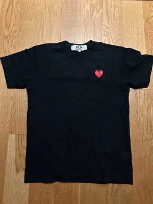 Svart Comme des Garçons Play t-shirt - Svart t-shirt från Comme des Garçons Play med det ikoniska röda hjärtat med ögon broderat på bröstet. Klassisk rund halsringning och korta ärmar. Tillverkad i mjuk bomull som känns skön mot huden. Perfekt för en clean och stilren look.