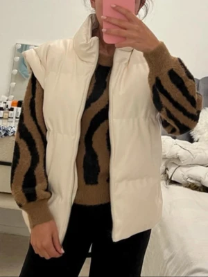 Vit dunväst med hög krage - Snygg vit dunväst med hög krage och breda axlar. Västen har en rak passform och stängs med dragkedja framtill. Perfekt att slänga över en tröja för en trendig lager-på-lager-look. Materialet är quiltat och ger en puffig känsla.