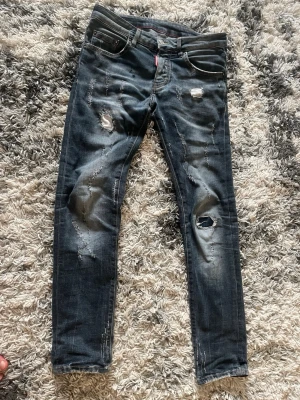 Mörkblå slitna skinny jeans - Säljer ett par mörkblå skinny jeans med slitningar och hål på benen för en trendig look. Jeansen har fem fickor, låg midja och detaljerade slitningar framtill. Perfekta för dig som gillar en avslappnad och edgy stil.