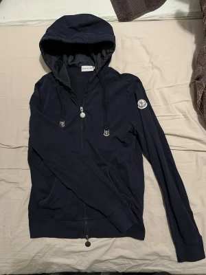 Moncler Maglia Cardigan - Säljer denna riktigt snygga och sällsynta moncler cardigan som är lite tunnare. Den har en nylon huva med dubbel zip, den passar mer åt Xs hållet. Givetvis är den äkta som syns i sista bilden✅ Hör av dig vid fler frågor och funderingar🙌