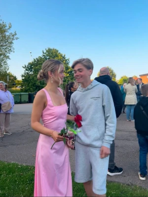 rosa långklänning med öppen rygg - Elegant rosa långklänning med breda axelband och öppen rygg med korsade band. Klänningen har en figurnära passform upptill och faller mjukt nedåt. Perfekt för sommarens speciella tillfällen. Jag är 161 cm lång, på bilen hade jag en liten klick också. Funkar både som Xs och S