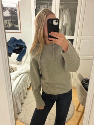 zara hoodie - Mysig grå stickad hoodie med huva och dragsko. Tröjan har breda ribbade muddar vid ärmslut och nederkant samt en avslappnad passform. Perfekt för en chill och stilren look. Materialet ser ut att vara mjukt och värmande, troligen ull- eller ullmix.