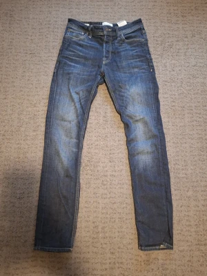 Mörk Blå jack & jones jeans - Säljer ett par mörk blåa Jack & Jones med passform slim fit och klassisk femficksdesign, Storlek 29W 32L. Jeansen har snygga slitningar och kontrastsömmar. Perfekta för dig som gillar en tidlös och enkel stil. Skrive vid frågor.
