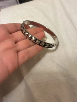 2 Edblad liknande Silvrigt armband med nitar - DU FÅR TVÅ FÖR 90kr SÄG TILL OM DU VILL HA EN SÅ FÅR DU DET FÖR 40kr! Snyggt armband i silverfärgad metall med kantiga nitar runt hela bandet. Armbandet har en rund form och ger en cool, edgy vibe till din stil. Perfekt för dig som gillar accessoarer med attityd och vill sticka ut lite extra.