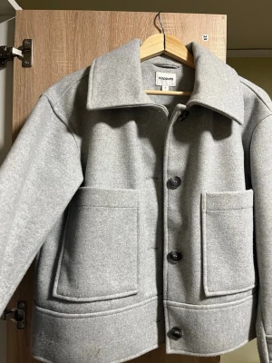 Ljusgrå ullkappa från Kappahl - Stilren ljusgrå kappa från Kappahl i ullmix med stora framfickor och bred krage. Kappan har knäppning med svarta knappar och rak passform som ger en modern look. Perfekt för dig som gillar minimalistisk och trendig stil. Aldrig använt bara testat  , priset går att diskutera