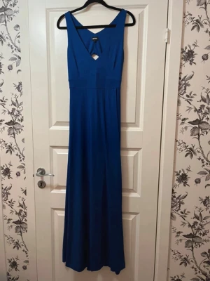 Blå långklänning med cut out - Snygg blå långklänning från NLY Eve med v-ringning och cut out-detalj framtill och baktill. Klänningen har breda axelband och är figurnära upptill med ett fallande kjolparti. Tillverkad i ett mjukt, stretchigt material som ger en bekväm passform. ☀️ Endast använd 1 gång på ett bröllop!