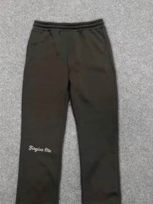 Mörkgröna mjukisbyxor med tryck - Mörkgröna mjukisbyxor med elastisk midja och sidofickor. På vänster ben står det 'Forgive Me' i vitt och baktill finns ett stort graffiti-inspirerat tryck. Perfekta för en chill och avslappnad stil.