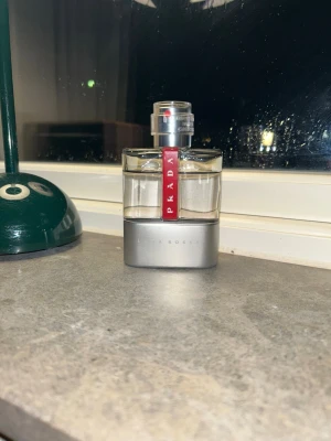 Prada Luna Rossa Eau de Toilette - Prada Luna Rossa är en elegant parfym i en stilren, genomskinlig glasflaska med silverfärgad botten och en röd vertikal detalj med Prada-loggan. Flaskan har en modern, maskulin design och känns lyxig och exklusiv – perfekt för dig som gillar klassiska dofter.