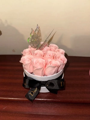 Evighetsrosor i box med fjäril - Säljer en rund vit ask fylld med ljusrosa konstgjorda rosor och dekorerad med en glittrig fjäril på toppen. Asken har en svart rosett med gulddetaljer med elegant band. Perfekt som present eller inredningsdetalj.