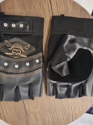 Svarta, punk handskar - Punk. Ett par fingerlösa handskar i svart med nitar och ett döskallemotiv. Handskarna har en justerbar rem runt handleden för en säker passform. Storlek 10,5 cm bred. Längd 17 cm. Polyester.