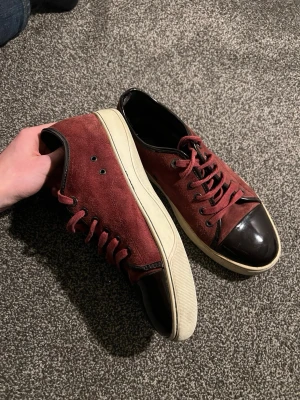 Lanvin Sneakers – Vinröd/Black Toe – Storlek 42-43 - 💥 Säljer ett par unika Lanvin-sneakers i vinrött med svart glansigt tåparti. 	•	Mockaliknande ovandel 	•	Matchande vinröda skosnören 	•	Vit sula med svarta detaljer 	•	Perfekta för dig som vill sticka ut med stil  Skick: Bra, men lädret inuti börjar lossna (rekommenderas svart strumpa). Lite heeldrag på sulan, men inget som stör looken.  Säljes för 1750kr 