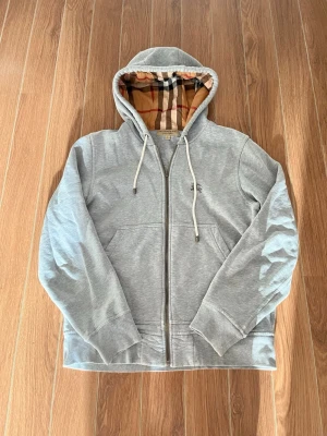 Grå zip hoodie från Burberry - Säljer en grå snygg zip hoodie från Burberry! Skick 7/10 bra skick men finns några små detaljer se de 3 sista bilder! Priset är därav de detaljer! Storlek S! Skriv till mig vid intresse eller frågor! MVH 🤗