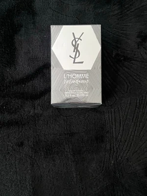 YSL L'Homme Eau de Toilette 100ml - YSL L'Homme Eau de Toilette 100ml i elegant silverfärgad förpackning med grafiskt mönster och tydlig YSL-logga. En klassisk herrparfym som kombinerar fräschör och maskulina toner. Perfekt för dig som gillar exklusiva dofter och snygg design.