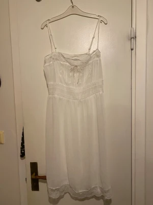 Vit klänning med spets och broderi💕 - Romantiskt vit klänning med tunna justerbara axelband, spetsdetaljer upptill och nertill samt broderade blommor på bröstet. Dekorativ rosett framtill och mjukt, luftigt tyg som ger en skön känsla. Perfekt för dig som gillar en söt och klassisk stil. Notera att den är väldigt genomskinlig så man behöver bära något under den💕😀