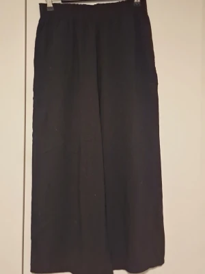 Svarta vida byxor  - Säljer ett par svarta byxor med breda ben och resår i midjan. Byxorna har en avslappnad passform och är perfekta för dig som gillar en enkel och stilren look. Materialet känns lätt och luftigt.
