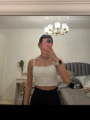 Vit croppad linnetopp med spets - Söt vit croppad linnetopp med tunna axelband och spetsdetaljer längs kanterna. Toppen har en lätt volang vid bysten och är perfekt för varma dagar. Enkel och stilren design som passar till mycket.