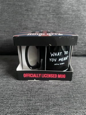 Justin Bieber svart mugg - Säljer en svart samlarmugg med texten 'What do you mean?' och Justin Bieber tryckt på framsidan. Muggen är officiellt licensierad och levereras i originalförpackning med brittisk flagga på locket. Perfekt för fans eller som present.