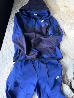 Blå tracksuit från Nike - Säljer en blå tracksuit från Nike med dragsko i midjan och klassisk vit Nike-logga på benet. Byxorna har en avslappnad passform och är gjorda i mjukt bomullsmaterial, perfekta för chill dagar eller träning.