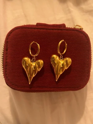WOS- Guldiga örhängen med hjärtan  - Säljer ett par statement örhängen i guldtonad metall med stora, droppformade hjärtan från WOS. Aldrig använda. 