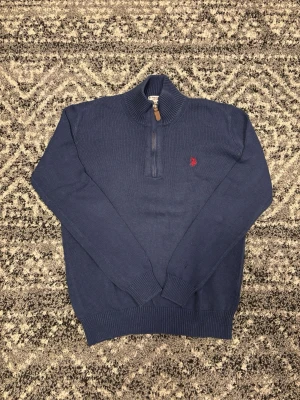 Marinblå stickad tröja med halv dragkedja - Snygg marinblå stickad tröja med halv dragkedja. Tröjan har en liten röd broderad logga på bröstet och hög krage. Tröjan är i storlek M. Hör av er vid eventuella frågor eller funderingar!! Pris går att diskutera!!