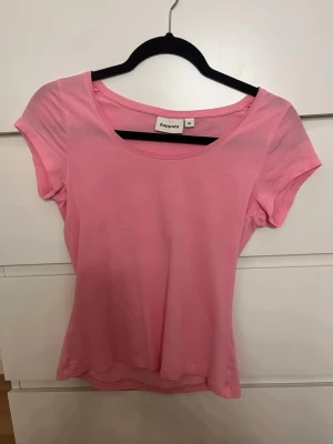 Rosa t-shirt från Kappahl - En enkel och snygg rosa t-shirt från Kappahl med rund halsringning och korta ärmar. Tillverkad i mjuk bomull som känns skön mot huden. Perfekt att matcha med jeans eller kjol för en avslappnad look.