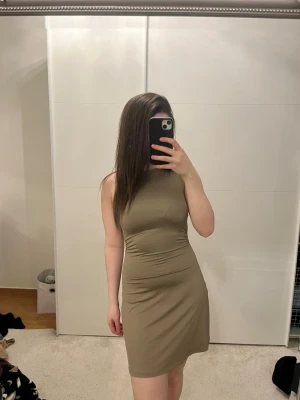 Beige ärmlös kort klänning - Säljer en enkel och stilren beige klänning i kort modell. Klänningen är ärmlös med en hög halsringning och har en figurnära passform som framhäver siluetten. Perfekt för dig som gillar minimalistisk och clean stil.