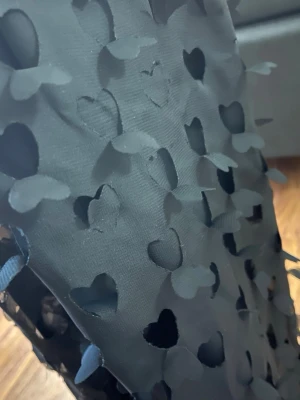 Svart sjal med hjärtdetaljer - Säljer en svart sjal med utstansade hjärtan och 3D-effekt på detaljerna. Sjalen är tunn och har en mjuk, flowy känsla som gör den enkel att styla till olika outfits. Perfekt accessoar för dig som gillar unika detaljer och en lekfull touch.