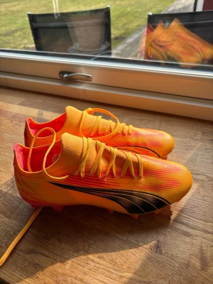 Puma orange fotbollsskor - Snygga fotbollsskor från Puma i en grymt fräsch orange och gul färg med svarta detaljer. Skorna har snörning, låg profil och rosa dobbar för bra grepp på planen. Tillverkade i syntetmaterial för lätt känsla och snabbhet. Nästan som nya, endast använt ett fåtal gånger❣️