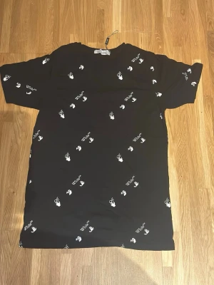 Svart t-shirt från Off-White - Säljer en svart t-shirt från Off-White med vitt tryck över hela plagget. T-shirten har korta ärmar och en relaxed passform. Materialet känns som mjuk bomull och trycket består av Off-White-loggor och små grafiska symboler.