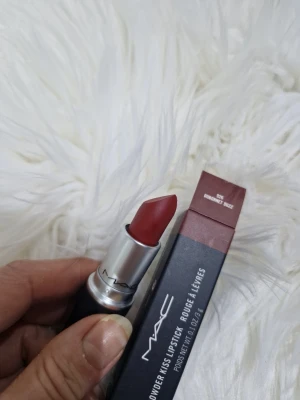 MAC Powder Kiss Dubonnet Buzz - MAC Powder Kiss Lipstick i färgen 926 Dubonnet Buzz. Ett matt läppstift i en djup rödbrun nyans med sammetslen finish. Hylsan är svart med silverdetaljer och klassisk MAC-design. Perfekt för dig som vill ha en mjuk, suddad look på läpparna.