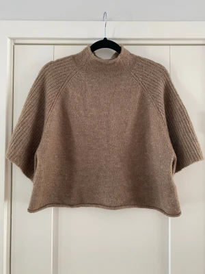 Beige stickad ponchotröja med halvpolo Pieces - Säljer en beige stickad ponchotröja med halvpolo och vida, ribbstickade ärmar. Tröjan har en avslappnad passform och är gjord i mjukt material, perfekt för lager på lager. Enkel och stilren design som passar till det mesta.Brun stickad tröja med hög krage och vida ärmar. Tröjan har en kortare, croppad modell.  Modell pcjuna bat wing cropped knit bc   Endast använd vid ett par tillfälle och i fint begagnat skick.  Mått Över bröstet: ca 54 cm Längd från axeln och ner: ca 49 cm  