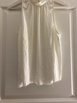 Vit ärmlös linnetopp med hög krage - Stilren vit topp med hög krage och knapp i nacken. Toppen är ärmlös och har en lätt rynkad detalj framtill, den är avklippt då jag tyckte den var för lång.💕