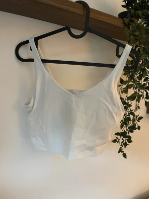 Vit träningstopp från RELODE  - Säljer en enkel och stilren vit TRÄNINGSTOPP från RELODE. Toppen är ärmlös med breda axelband och har en något croppad passform. 