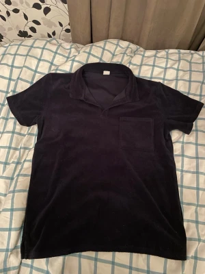 Mörkblå kortärmad topp från Lindex - Mörkblå kortärmad topp från Lindex med mjuk frottéstruktur. Toppen har en klassisk krage, bröstficka och relaxed fit. Perfekt för dig som gillar en enkel men ändå stilren look.