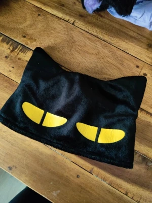 Svart kattmössa med gula ögon från trigun anime  - Säljer en svart mössa i mjukt tyg med kattöron och två gula kattögon framtill. Mössan har en unik och lekfull design som sticker ut och passar perfekt för dig som gillar djurmotiv eller vill ha en rolig accessoar till din outfit.