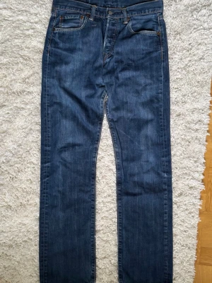 Levi's 501 jeans - Säljer ett par klassiska mörkblå jeans från Levi's med rak passform och fem fickor. Jeansen har den ikoniska röda Levi's-lappen bak och är tillverkade i slitstark denim. Perfekta för en avslappnad och tidlös stil. W31 L34
