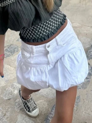 Jeanskjol med volang - Säljer en vit kortkjol med volang och ballongformad siluett. Kjolen har fickor fram och stängs med knapp och dragkedja. Perfekt för sommarens alla outfits och är tillverkad i bomull för en skön känsla.