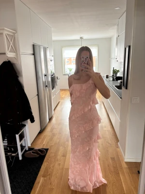 Ljusrosa långklänning med volanger - Supersöt ljusrosa långklänning med volanger. Jag är 168cm. Obs lite trasig vid höger höft, se bild 3. 