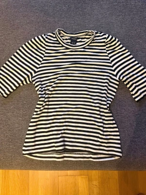 Randig topp från Lindex - Mjuk och stretchig randig topp i svart/vitt. Skönt fall tack vare viskos och följsam passform med elastan. Rund hals och 3/4-ärm. 95% viskos 5% elastan. Storlek XS. Fint skick. 