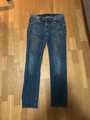 Raka jeans från J.Lindeberg - Säljer ett par blå jeans med rak passform och fem fickor. Jeansen har en klassisk midja och subtila slitningar för en avslappnad look. Tillverkade i denim, perfekta till vardagsstilen. Passar dig som gillar tidlös och enkel design.