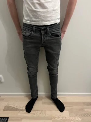 Grå slim fit jeans herr - Snygga grå slim fit jeans med fem klassiska fickor och dragkedjegylf. Jeansen har en smal passform som sitter tight längs benen och är perfekta för en modern stil. Materialet är stretchigt för extra komfort.